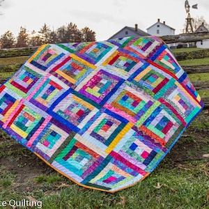 K&ouml;nnte beinhalten: Ein farbenfroher Quilt mit einem Blockhausmuster, der eine Vielzahl von leuchtenden Farben und Stoffen zeigt. Der Quilt ist &uuml;ber einen Holzzaun gelegt.