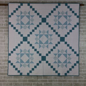 May include: A white quilt with a blue and white star pattern. The quilt is made with squares and has a diamond pattern in the center.