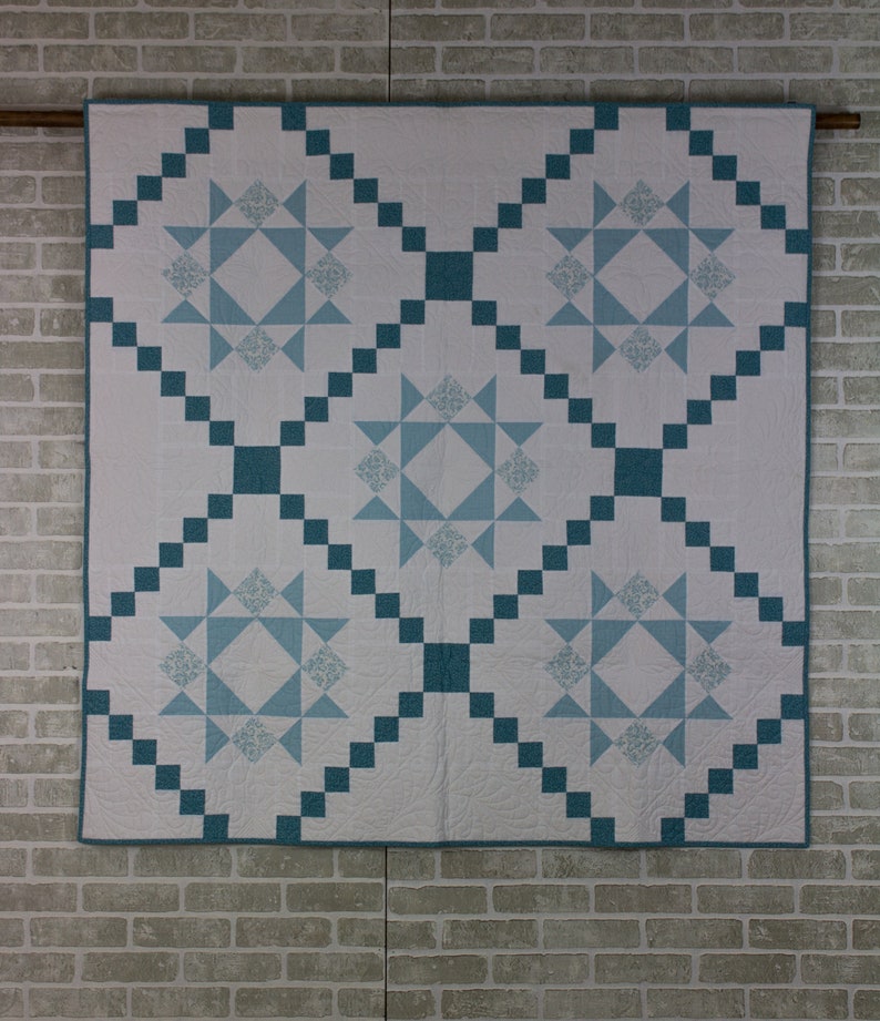 May include: A white quilt with a blue and white star pattern. The quilt is made with squares and has a diamond pattern in the center.