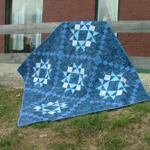 May include: A blue and white quilt with a star pattern. The quilt is made of fabric squares sewn together to create a geometric design.