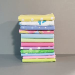May include: A stack of 14 fabric squares in various pastel colors and patterns, including polka dots, stripes, and floral designs.
