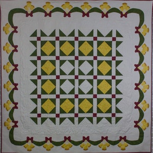 May include: A white quilt with a green and yellow diamond pattern in the center. The quilt is bordered by a green and red ribbon with yellow bells.