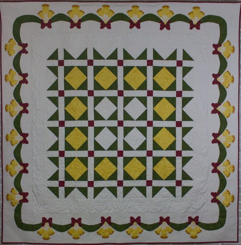 May include: A white quilt with a green and yellow diamond pattern in the center. The quilt is bordered by a green and red ribbon with yellow bells.