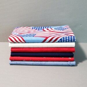 May include: A stack of six fabric squares in red, white, and blue colors. The top square features a pattern of American flags. The fabric squares are folded neatly.