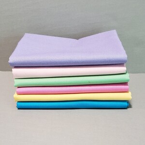 May include: A stack of six fabric squares in pastel colors, including lavender, pink, light green, light pink, yellow, and blue.