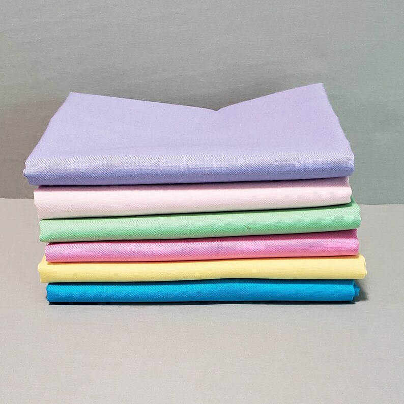 May include: A stack of six fabric squares in pastel colors, including lavender, pink, light green, light pink, yellow, and blue.