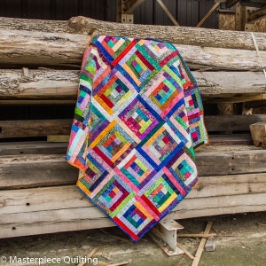 K&ouml;nnte beinhalten: Ein farbenfroher Quilt mit Patchwork-Muster aus Quadraten und Rechtecken in verschiedenen Rot-, Orange-, Gelb-, Gr&uuml;n-, Blau-, Lila- und Braunt&ouml;nen. Der Quilt h&auml;ngt an einer Holzwand.