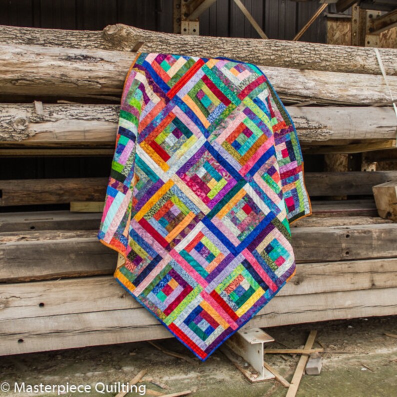 K&ouml;nnte beinhalten: Ein farbenfroher Quilt mit Patchwork-Muster aus Quadraten und Rechtecken in verschiedenen Rot-, Orange-, Gelb-, Gr&uuml;n-, Blau-, Lila- und Braunt&ouml;nen. Der Quilt h&auml;ngt an einer Holzwand.