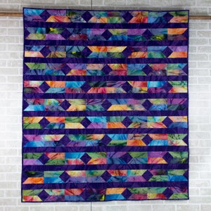 May include: A colorful quilt with a geometric pattern of diamonds and rectangles. The quilt is made of purple, blue, green, orange, and pink fabric.