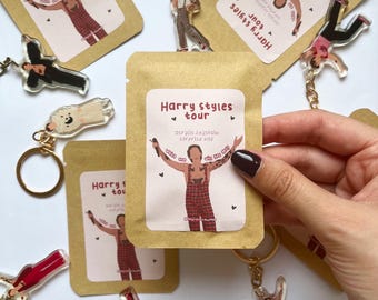 May include: A collection of Harry Styles tour-themed merchandise, including keychains and small paper packages. The keychains feature acrylic figures of Harry Styles in various poses. The packages have a label with the text "Harry Styles tour".