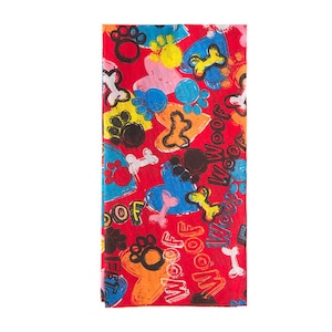 Puede incluir: Un pañuelo rectangular rojo con un patrón colorido de huellas de perro, huesos y corazones. La palabra "WOOF" está escrita en blanco. El diseño incluye elementos azules, amarillos, naranjas, rosas y negros.