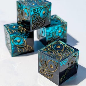 May include: A set of four translucent teal resin cubes featuring embedded gold-colored metallic eye-shaped patterns. Each cube has a smooth, polished finish with the intricate gold designs visible on the top and side faces of the geometric objects.