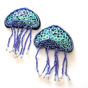 May include: Two blue and green beaded jellyfish with iridescent sequins and dangling blue beads.