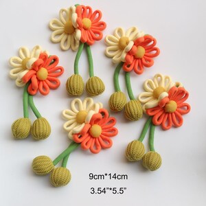 May include: Six handmade fabric flower embellishments with green yarn stems and two green yarn balls at the end of each stem. The flowers are a combination of cream and orange fabric. The flowers measure 9cm by 14cm.