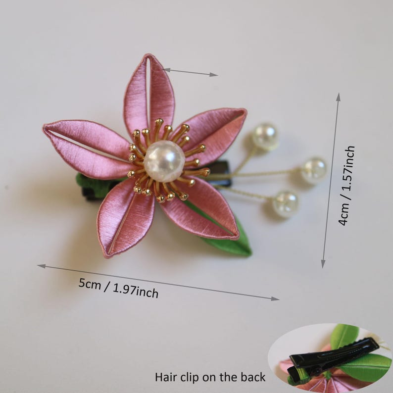 Puede incluir: Pinza para el pelo con forma de flor rosa con un centro de perla y tres adornos de perlas. La pinza mide 5 cm de largo y 4 cm de ancho. La parte trasera de la pinza es negra.