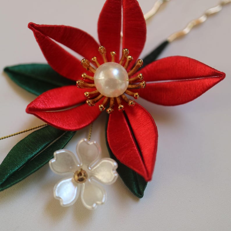 May include: A red silk flower with a pearl center and gold accents, with green leaves and a white flower with a pearl center.