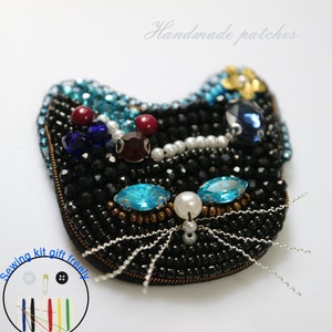 May include: Black beaded cat brooch with blue, red and white rhinestones. The cat has a white pearl nose and silver whiskers. The brooch is handmade and says "Handmade patches" at the top.