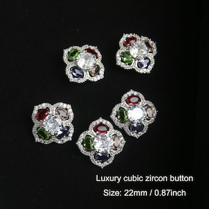 Puede incluir: Cuatro botones de plata en forma de flor con diamantes de imitación transparentes y de colores. Cada botón tiene un diamante de imitación central transparente rodeado de cinco diamantes de imitación ovalados en rojo, verde, azul y marrón. Los botones tienen un diámetro de 22 mm o 0,87 pulgadas. Botón de circonita cúbica de lujo.