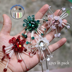 May include: Four sparkly, star-shaped embellishments with different colored centers: red, green, pink, and clear. Each embellishment has silver metal prongs radiating outward. The text "4pcs in pack" is visible in the lower right corner.
