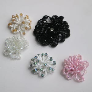 May include: Five beaded flower embellishments in various colors, including white, black, pink, and gold. The embellishments are made of small, round beads and have a delicate, floral design.