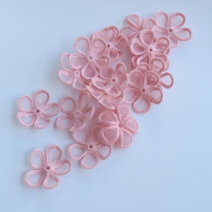 May include: A group of pale pink crocheted flower embellishments. The flowers are delicate and have a lacy appearance.