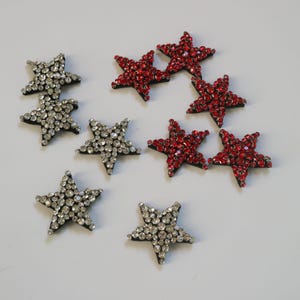 May include: Assortment of red and silver star-shaped embellishments with rhinestones. The stars are made of fabric and have a black backing.