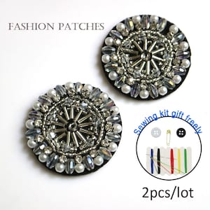Könnte beinhalten: Zwei runde Patches aus silbernen und weißen Perlen mit schwarzem Filzrücken. Die Patches haben einen Durchmesser von 5 cm und ein kreisförmiges Design mit einem Stern in der Mitte. Das Bild zeigt auch ein Nähset mit Nadeln, Garn, Knöpfen und einer Sicherheitsnadel. Der Text "Sewing kit gift freely" und "2pcs/lot" ist auf dem Bild zu sehen.