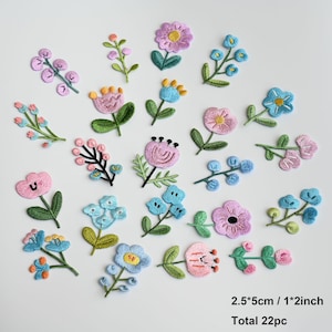 May include: A collection of 22 embroidered flower patches in various shades of pink, blue, and green. Each patch features distinct floral designs with stems and leaves. The text 2.5*5cm / 1*2inch and Total 22pc is printed in the bottom right corner.