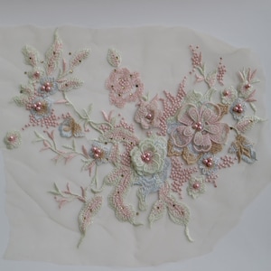 May include: A delicate floral applique featuring pink, white and green embroidery with pearl accents. The applique is ideal for adding a touch of elegance to clothing, accessories or home decor.