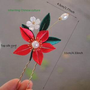 May include: Red and green silk flower hair pin with a pearl accent. The pin is 4.33 inches long and 1.77 inches wide.  "Inheriting Chinese culture" is written in green text on the image.