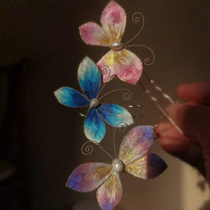 May include: Three butterfly hair pins with delicate wire antennae and pearl accents. The butterfly wings are painted in shades of pink, blue, and purple with gold detailing. These decorative hair accessories are perfect for special occasions.
