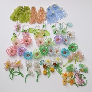 Puede incluir: Surtido de pendientes de flores de cuentas de colores. Los pendientes están hechos con cuentas pequeñas y presentan una variedad de formas y colores de flores, incluyendo rosa, azul, verde, amarillo y blanco.