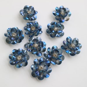 Könnte beinhalten: Zehn blaue, schillernde, blumenförmige Verzierungen mit einem klaren Strassstein in der Mitte.