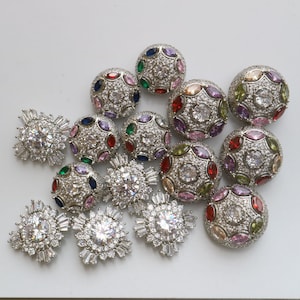 May include: Assortment of silver-toned, round, decorative buttons with colorful gemstones and clear rhinestones. The buttons have a variety of designs and are perfect for adding a touch of sparkle to any project.