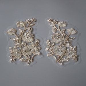 May include: Two gold floral appliques with pearl and crystal embellishments on a sheer fabric background.