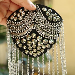 Könnte beinhalten: Ein schwarzer Stoff-Patch mit silberfarbenen Nieten und Strasssteinen, akzentuiert mit herabhängenden silbernen Ketten.