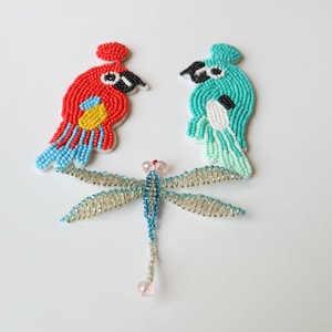 May include: Three beaded animal figures: a red and blue parrot, a turquoise and white parrot, and a blue dragonfly with a pink body.