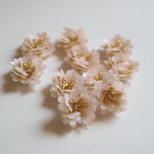 Könnte beinhalten: Zehn zarte rosa Stoffblumenverzierungen mit goldenen und klaren Strasssteinen.