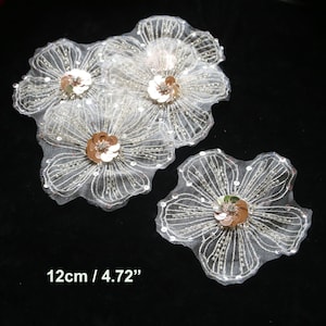 Peut inclure: Quatre appliques en tissu de forme florale blanches avec un design perlé et un centre de paillettes dorées. Chaque applique mesure 12 cm / 4,72 pouces.