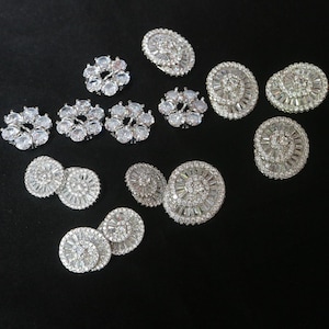 May include: Assortment of silver-toned rhinestone embellishments in various shapes and sizes. The embellishments are perfect for adding sparkle to crafts, clothing, and accessories.