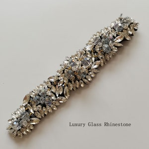 May include: A black ribbon adorned with a cluster of clear glass rhinestones. The rhinestones are arranged in a cascading pattern, creating a luxurious and elegant look. "Luxury Glass Rhinestone" is written below the ribbon.