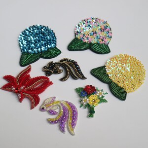 May include: Assortment of colorful beaded flower and fish brooches. The brooches are made with sequins and beads in various colors, including red, blue, yellow, green, and purple. The brooches are perfect for adding a touch of whimsy to any outfit.