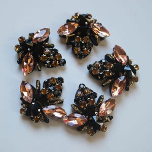 May include: Four bee-shaped decorative patches featuring black fabric bases, peach-coloured marquise-cut crystals for wings, and small amber-toned round rhinestones and metallic gold-tone beads accenting the bodies and heads of the insects.