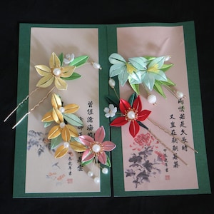 May include: Set of five handmade silk flower hair pins. The pins feature delicate flowers in shades of green, yellow, pink, and red with pearl accents. The pins are displayed on a card with Japanese calligraphy.