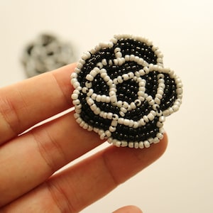 Könnte beinhalten: Eine schwarze und weiße Perlenblume mit einem 3D-Design. Die Blume besteht aus kleinen, runden Perlen, die zusammengenäht sind, um eine Rosenform zu bilden.