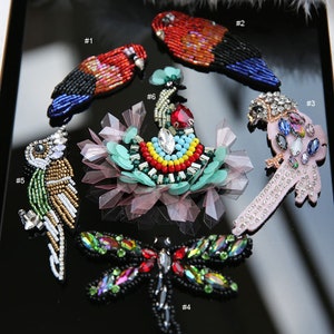 May include: Six colorful beaded appliques, including a dragonfly, a peacock, and four different birds. The appliques are numbered 1 through 6.