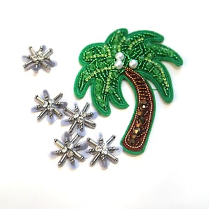 May include: Embroidered palm tree and starburst embellishments. The palm tree is green with a brown trunk and pearl accents. The starbursts are silver and clear with a light purple backing. These are likely for clothing or craft projects.
