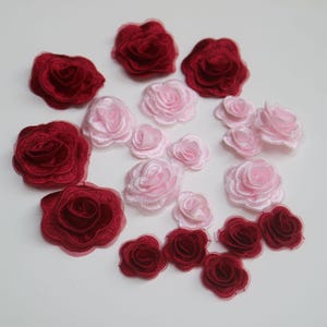 May include: Assortment of pink and burgundy fabric rose embellishments. The roses are layered and have a delicate, ruffled texture.