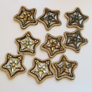May include: Nine star-shaped embellishments with a variety of crystal colours and designs. The embellishments are made of a gold-toned metal and have a raised, textured surface.