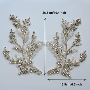 Könnte beinhalten: Zwei symmetrische florale Applikationen mit klaren Strasssteinen und silberner Metallfadenstickerei auf einem transparenten Netzstoff. Die Teile messen 26,5 cm in der Höhe und 16,5 cm in der Breite, wie durch den Text und die Pfeile angegeben.